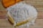 A pile of white flour sits on a wooden surface, accompanied by a wooden scoop and two sprigs of wheat.