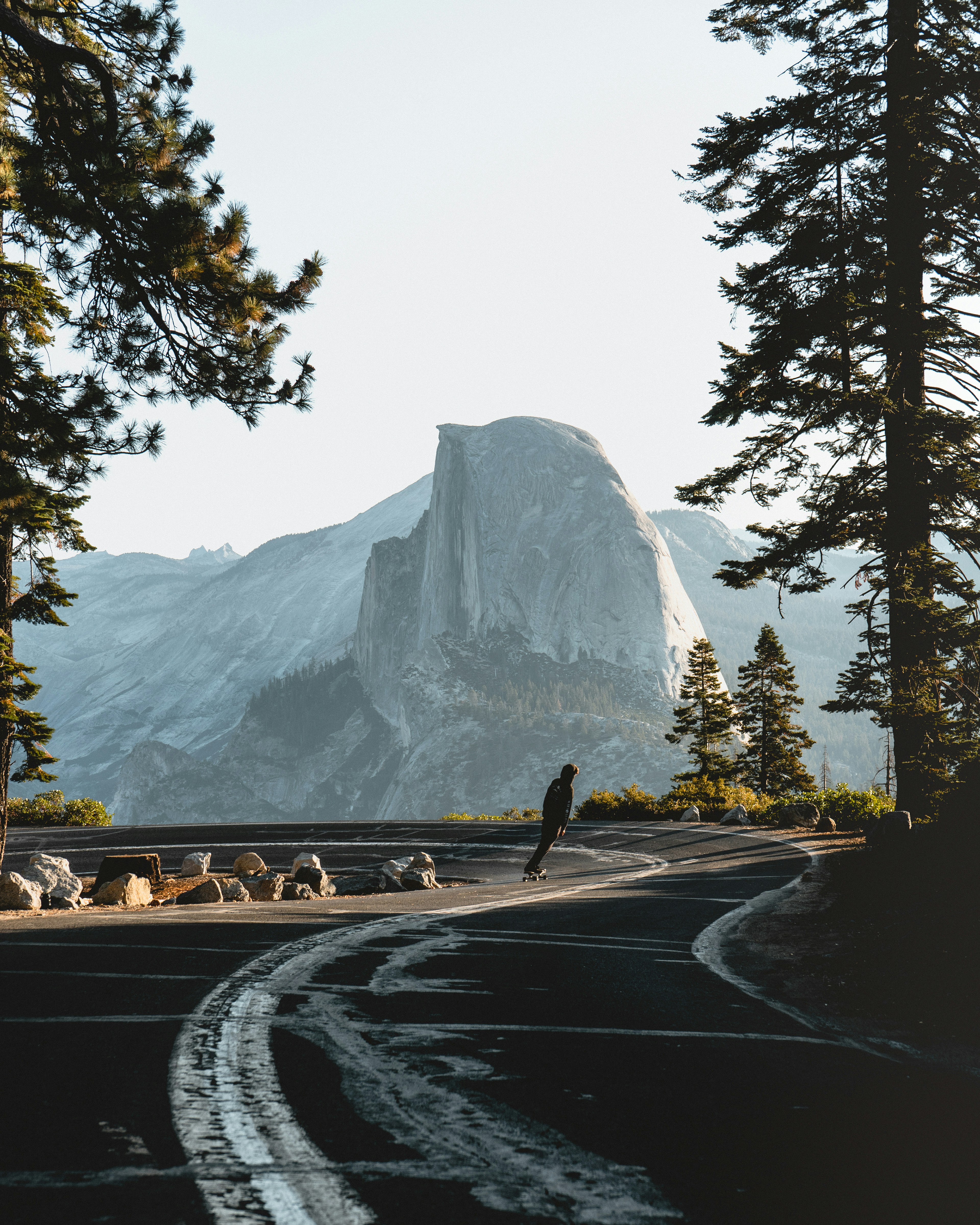 gray concrete road near green trees and mountain during daytime