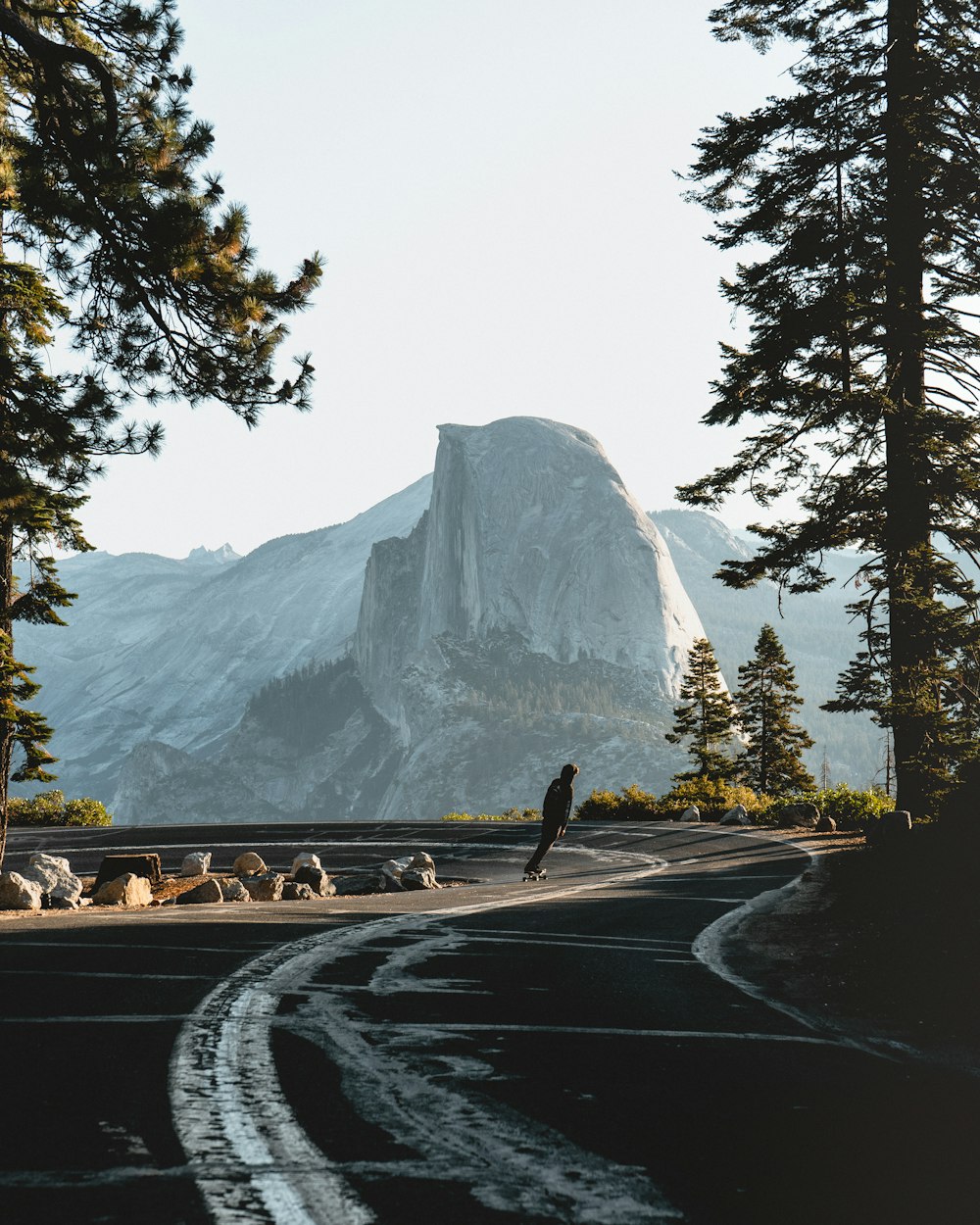 gray concrete road near green trees and mountain during daytime