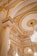 An opulent interior featuring ornate golden decorations and intricate architectural details. The ceiling is adorned with elaborate gold patterns, and a large, elegant chandelier hangs prominently. There are several columns with gold accents, enhancing the luxurious atmosphere.