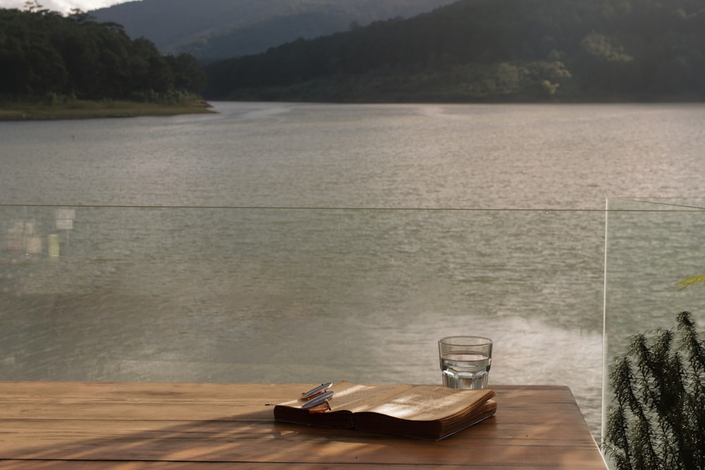 copo de beber transparente na mesa de madeira marrom perto do corpo de água durante o dia