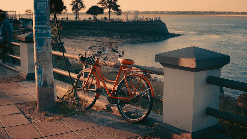 brown city bike parked beside white concrete post near body of water during daytime