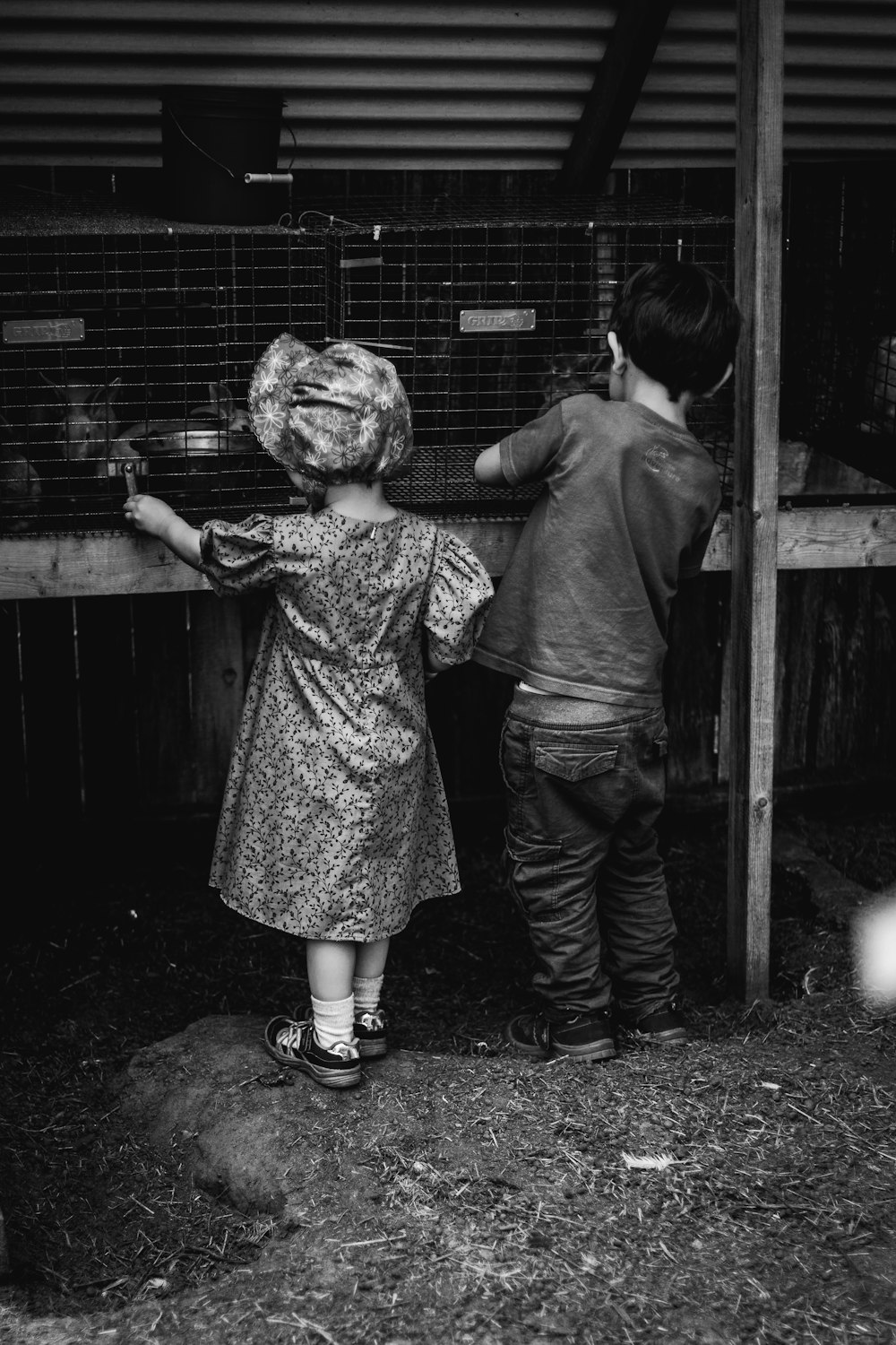 Foto en escala de grises de 2 niños parados al lado de la valla