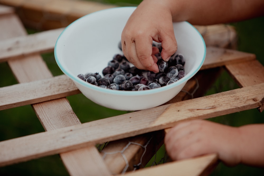 person holding blue berries in white ceramic bowl