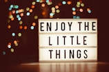a lit up sign that says enjoy the little things