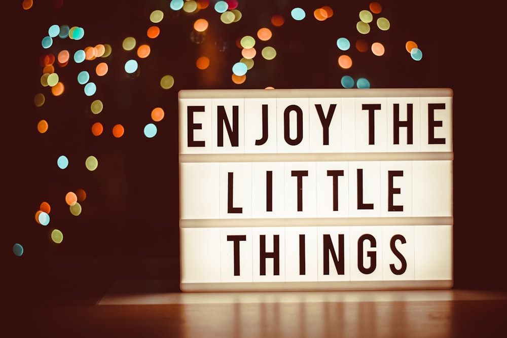 a lit up sign that says enjoy the little things