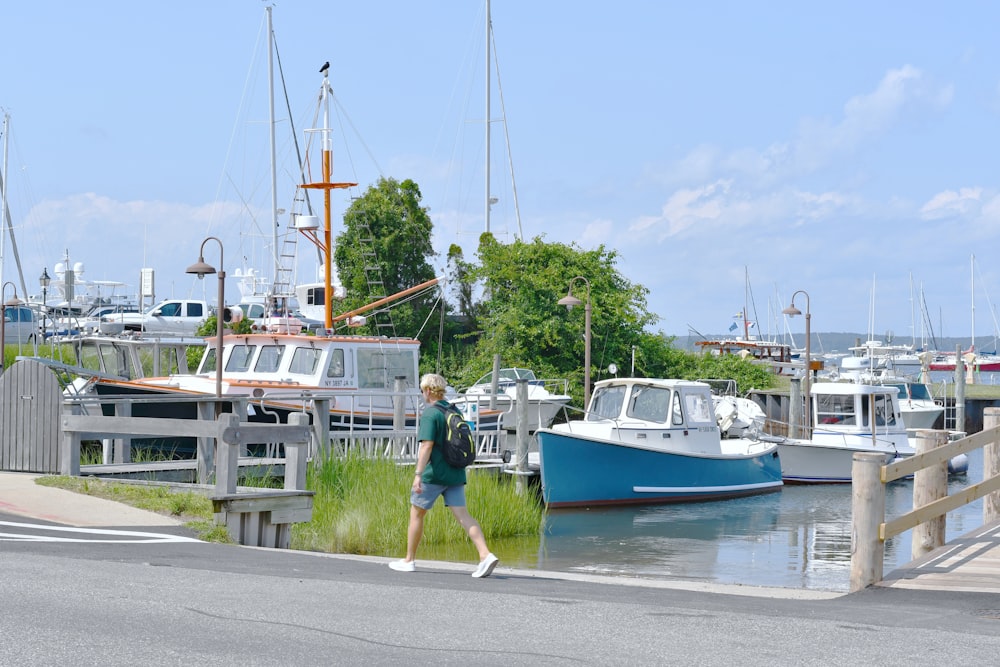 昼間、白と青のボートの近くの通りを歩く緑のシャツを着た男性