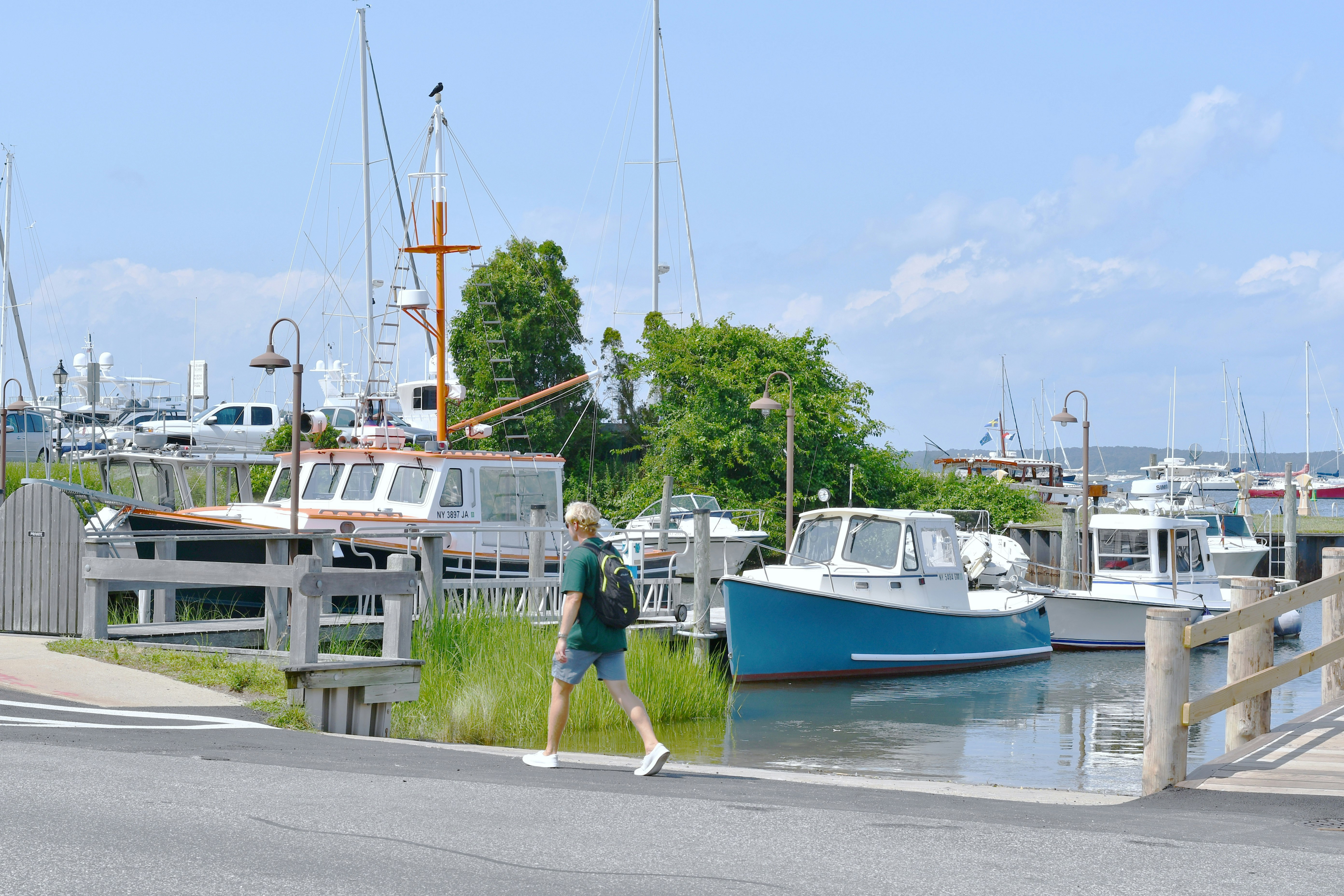 man in green shirt walking on the street near white and blue boat during daytime