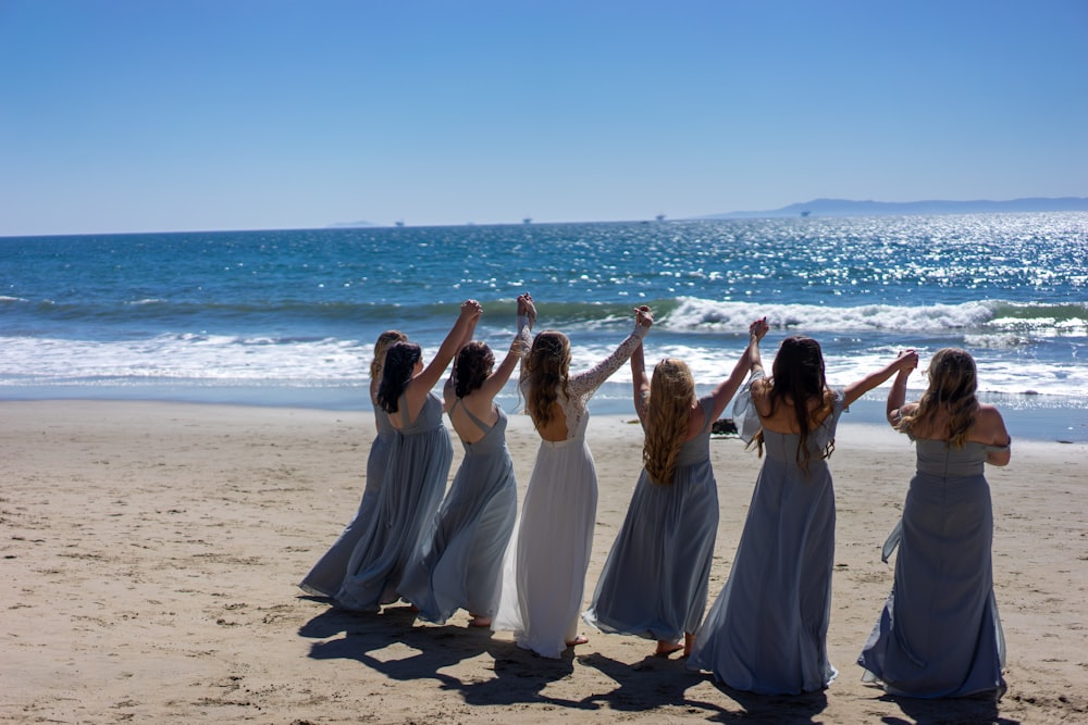 Mujeres con vestidos blancos de pie sobre arena marrón cerca del cuerpo de agua durante el día