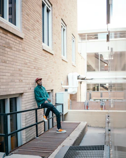 Man adjusting the collar of his jacket while leaning against a graffitied wall in an urban alley.