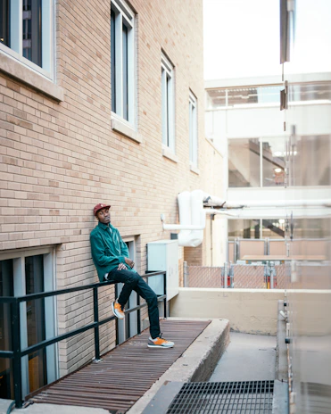 Man adjusting the collar of his jacket while leaning against a graffitied wall in an urban alley.