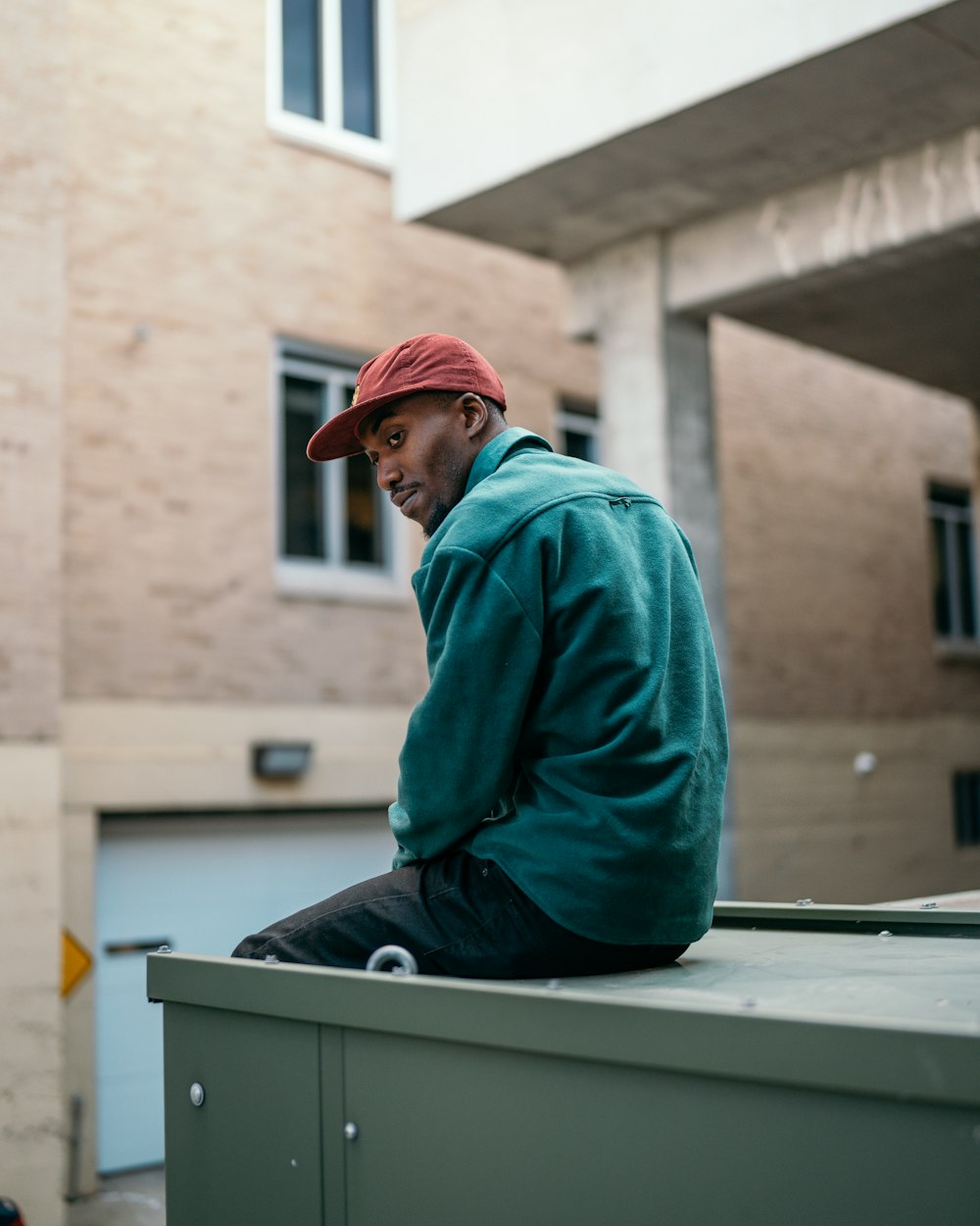 Hombre con sudadera con capucha azul y gorra roja sentado en un banco blanco