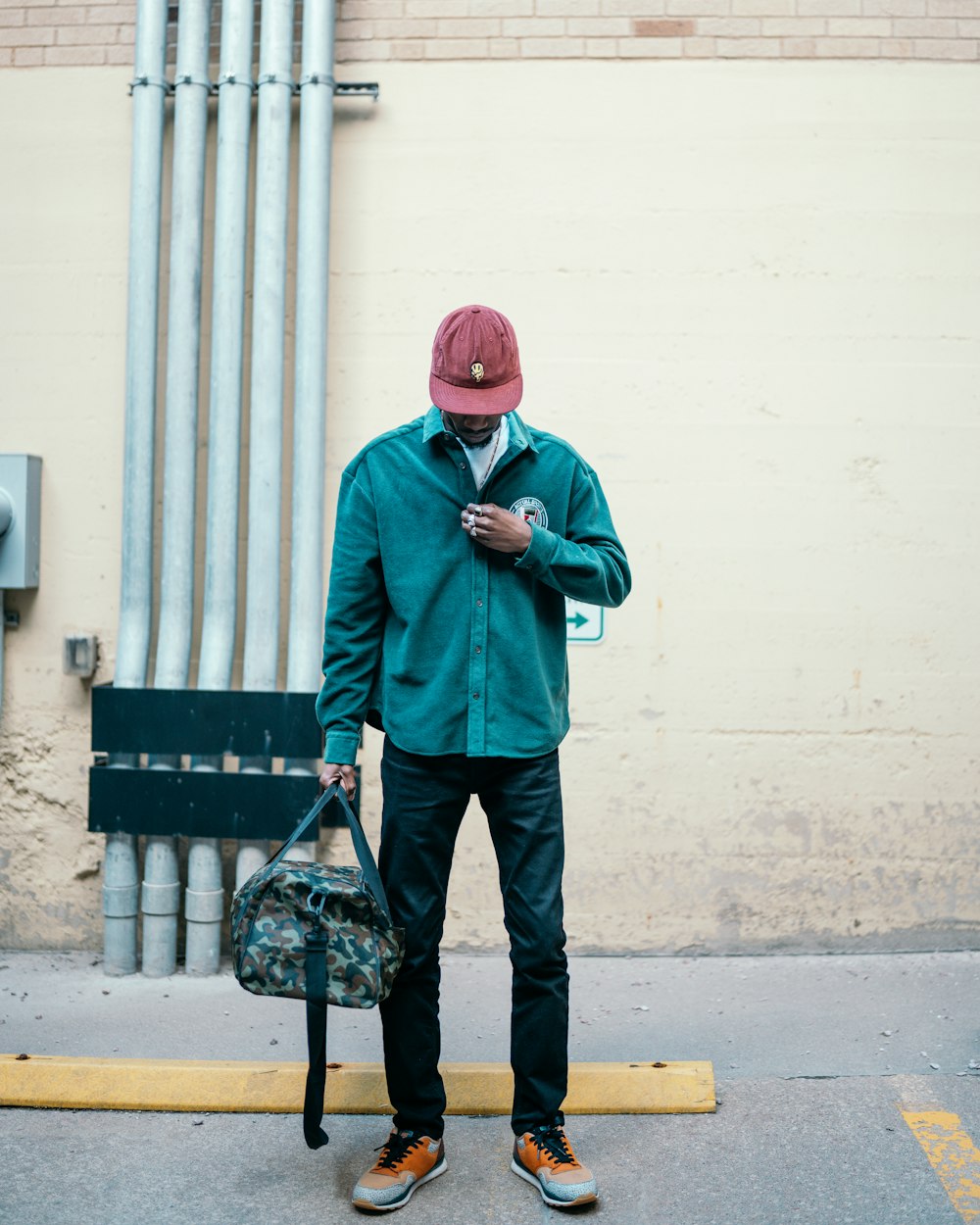 Hombre con chaqueta verde y pantalones negros con máscara roja de pie junto a la pared blanca durante el día