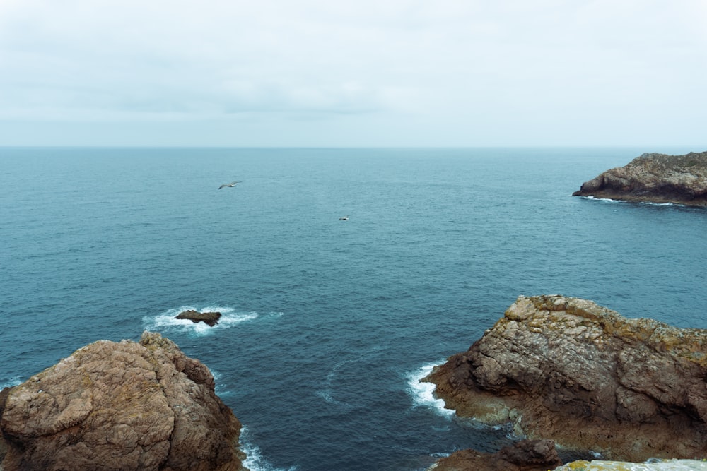 brauner felsiger Berg neben blauem Meer unter weißem Himmel tagsüber