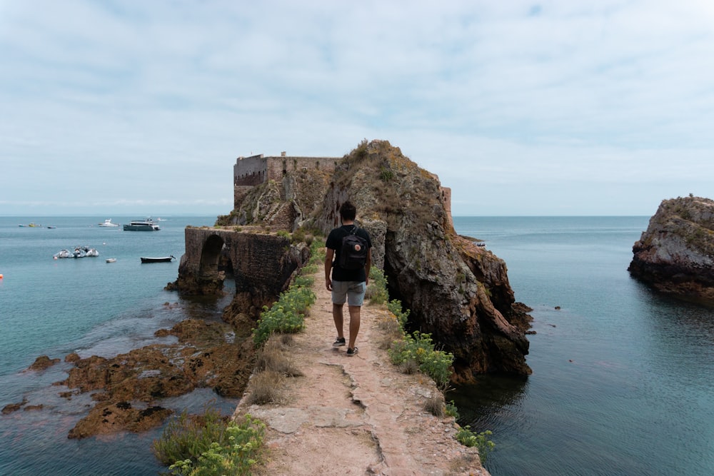 man in black t-shirt and brown shorts standing on brown rock formation near body of on on on on