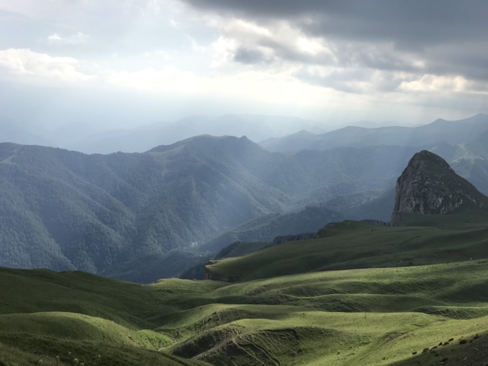 green grass field and mountains under white clouds and blue sky during daytime