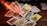 A hand with painted nails holds up a tarot card above a wooden table scattered with various other tarot cards. Some cards are face up, displaying intricate and colorful designs, while others are face down. The lighting is warm, creating a mystical and intimate atmosphere.