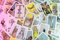 A collection of Tarot cards is scattered across a surface, displaying a variety of illustrations and symbolism. Some cards are upright, while others are upside down, featuring figures such as 'The Hanged Man,' 'The Sun,' 'The Fool,' and 'The Devil.' The cards are colorful and intricately designed, often depicting medieval or mythical scenes with characters, animals, and symbolic objects.