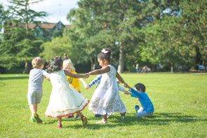 A group of children holding hands in a circle on a sunny park lawn