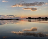A peaceful sunset over a calm lake with soft reflections on the water.