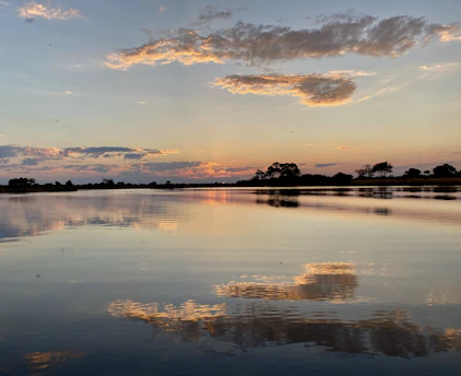 A serene sunset over a calm lake reflecting soft orange and pink hues.