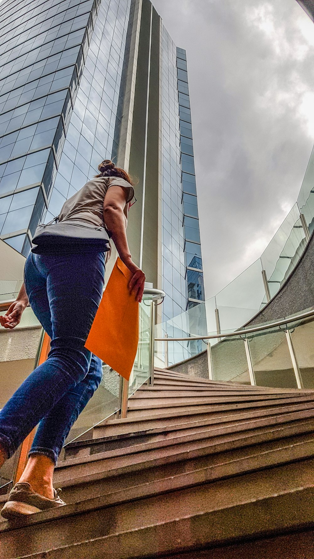 Mujer con camiseta gris y jeans de mezclilla azul de pie en escaleras de madera marrón