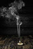 A cone-shaped incense burner sits on a wooden surface with smoke gracefully rising in swirling patterns against a dark background.
