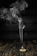 A cone-shaped incense burner sits on a wooden surface with smoke gracefully rising in swirling patterns against a dark background.