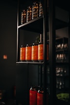 A shelving unit displays multiple rows of canned beverages. The cans on the top shelf are labeled 'UNA IPA' with a predominantly black color scheme. The middle shelf holds orange-labeled cans with 'Mango Sour' printed on them. The lower shelf features another set of cans with a red design and 'Peach Sour' text.