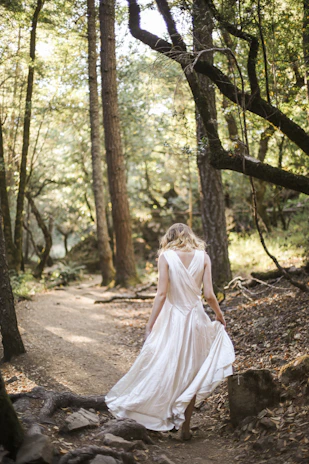 A candid shot of a woman in a flowing white dress walking through a sunlit urban park.