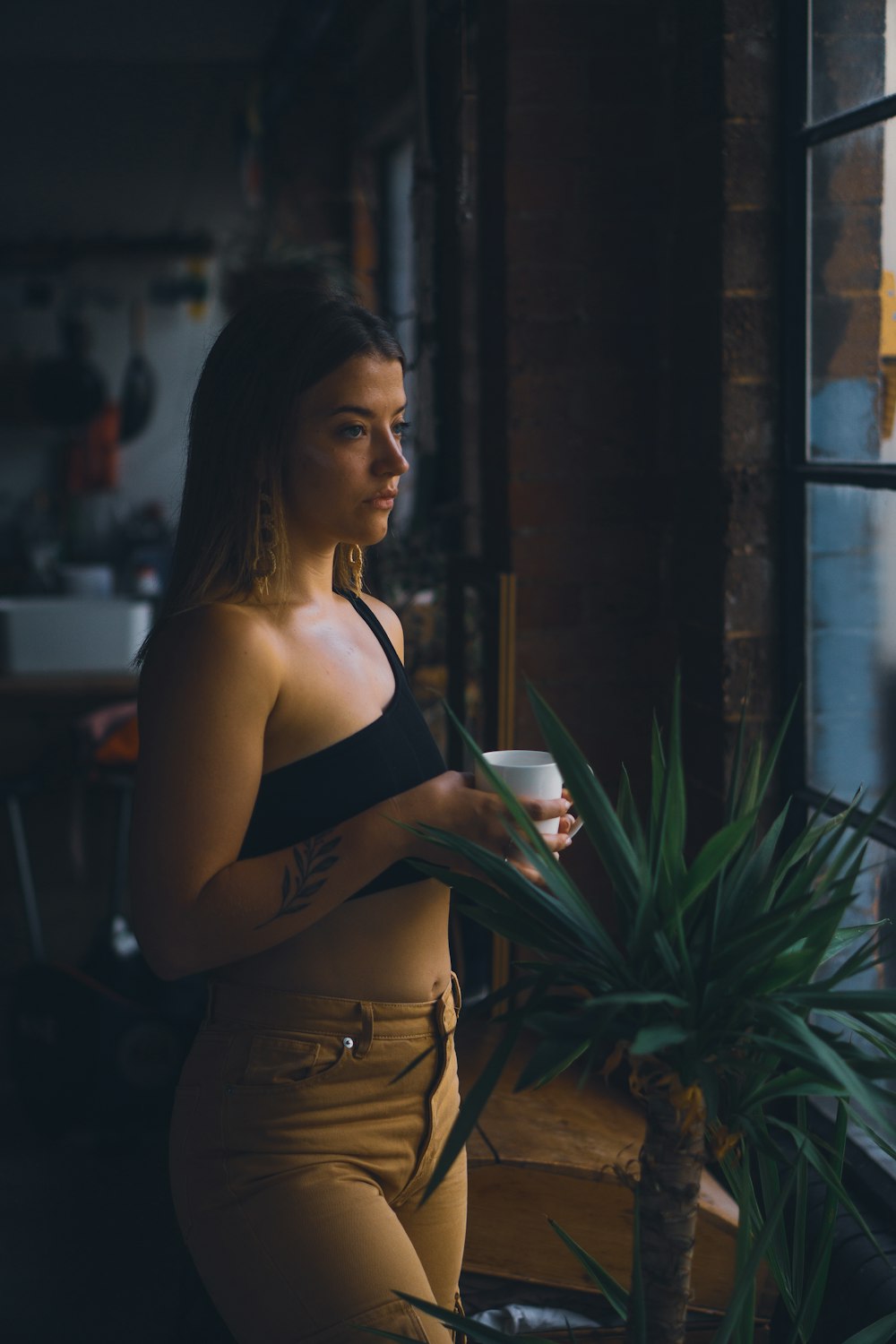 woman in black brassiere and brown pants standing near green plant