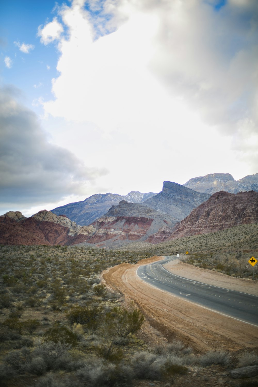 gray asphalt road near brown mountains under white cloudy sky during daytime