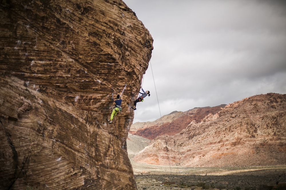 man in green jacket and blue pants climbing on brown rock mountain during daytime