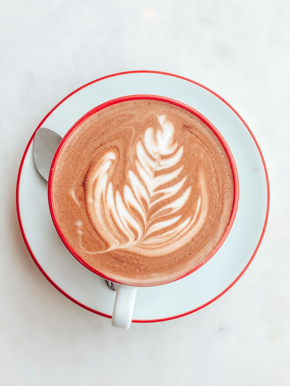 white and red ceramic mug with brown and white heart shaped coffee art