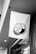 A monochrome image featuring a fabric sign hanging from a bracket. The sign displays a round logo with the words 'Press the Button Coffee Stand', surrounded by artistic shading.