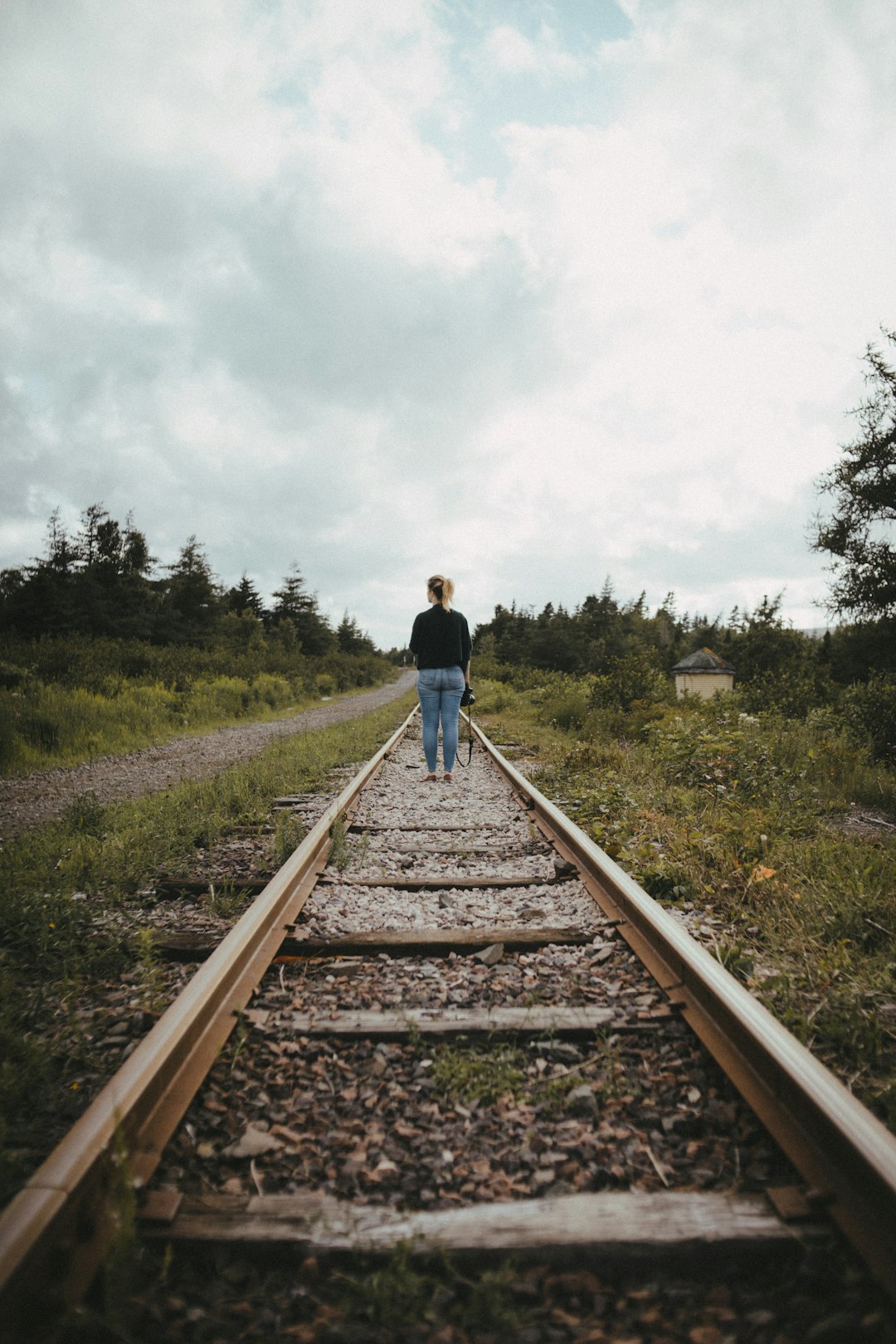 woman in blue jacket walking on brown train rail during daytime