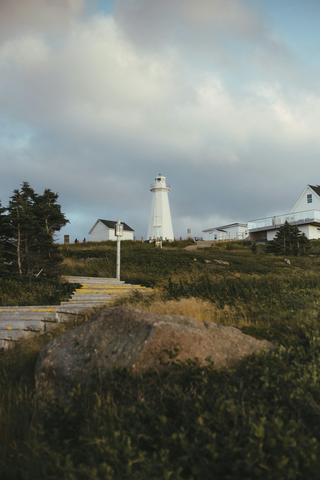 white lighthouse near green trees under white clouds during daytime