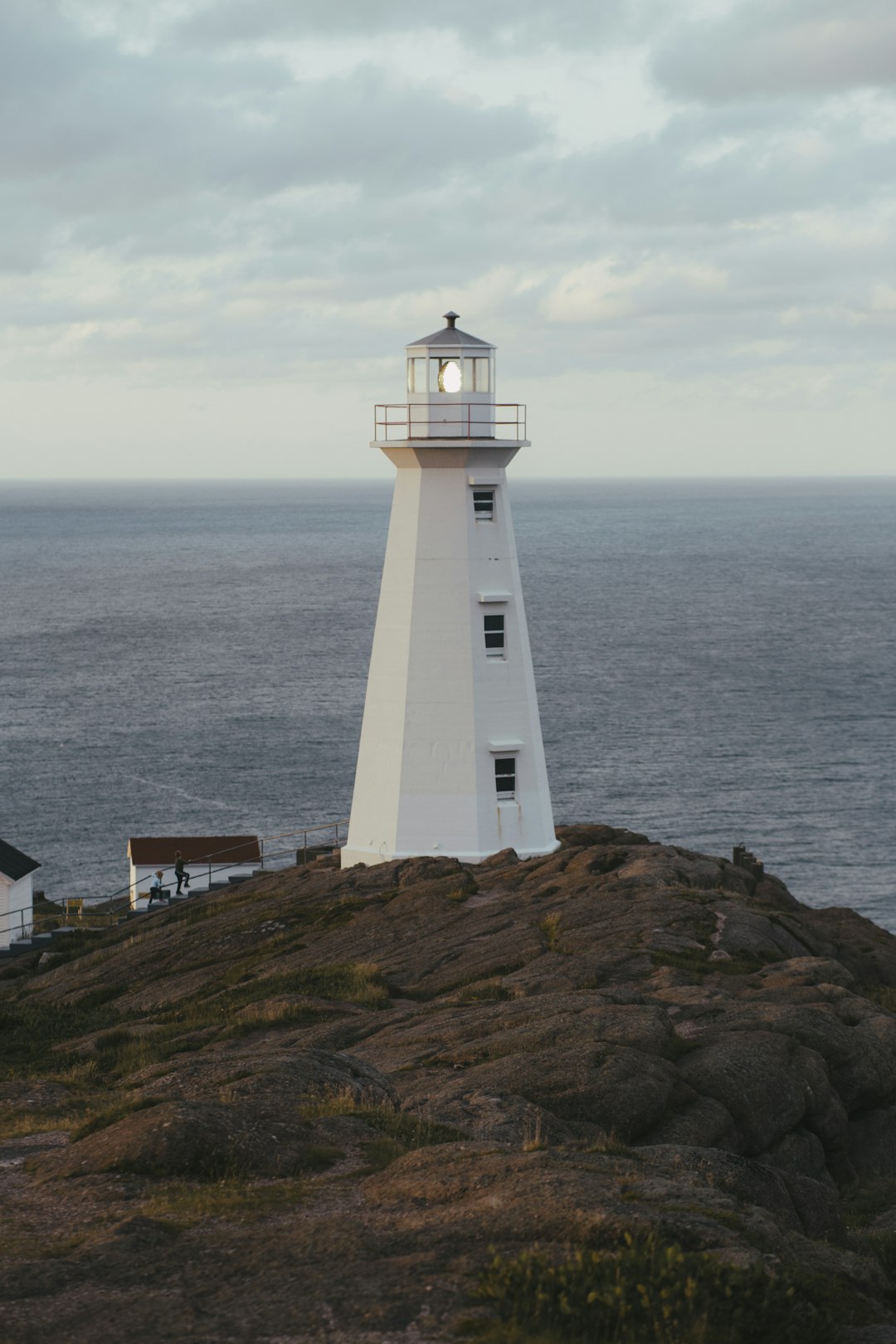 white lighthouse on brown hill near body of water during daytime