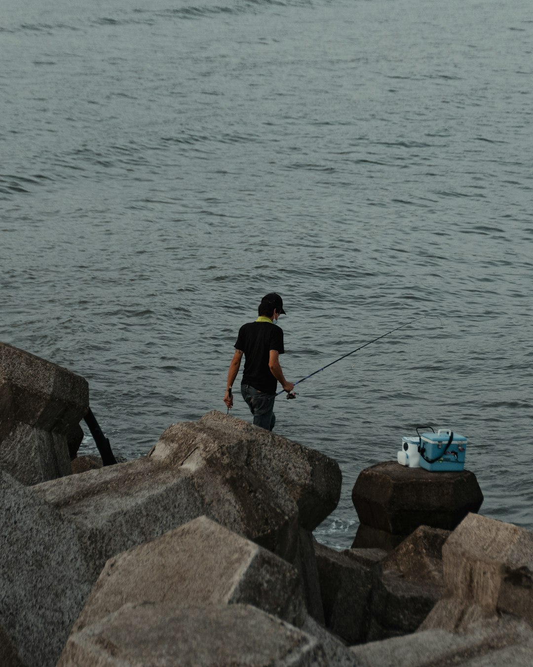 man in black t-shirt and black shorts fishing on sea during daytime