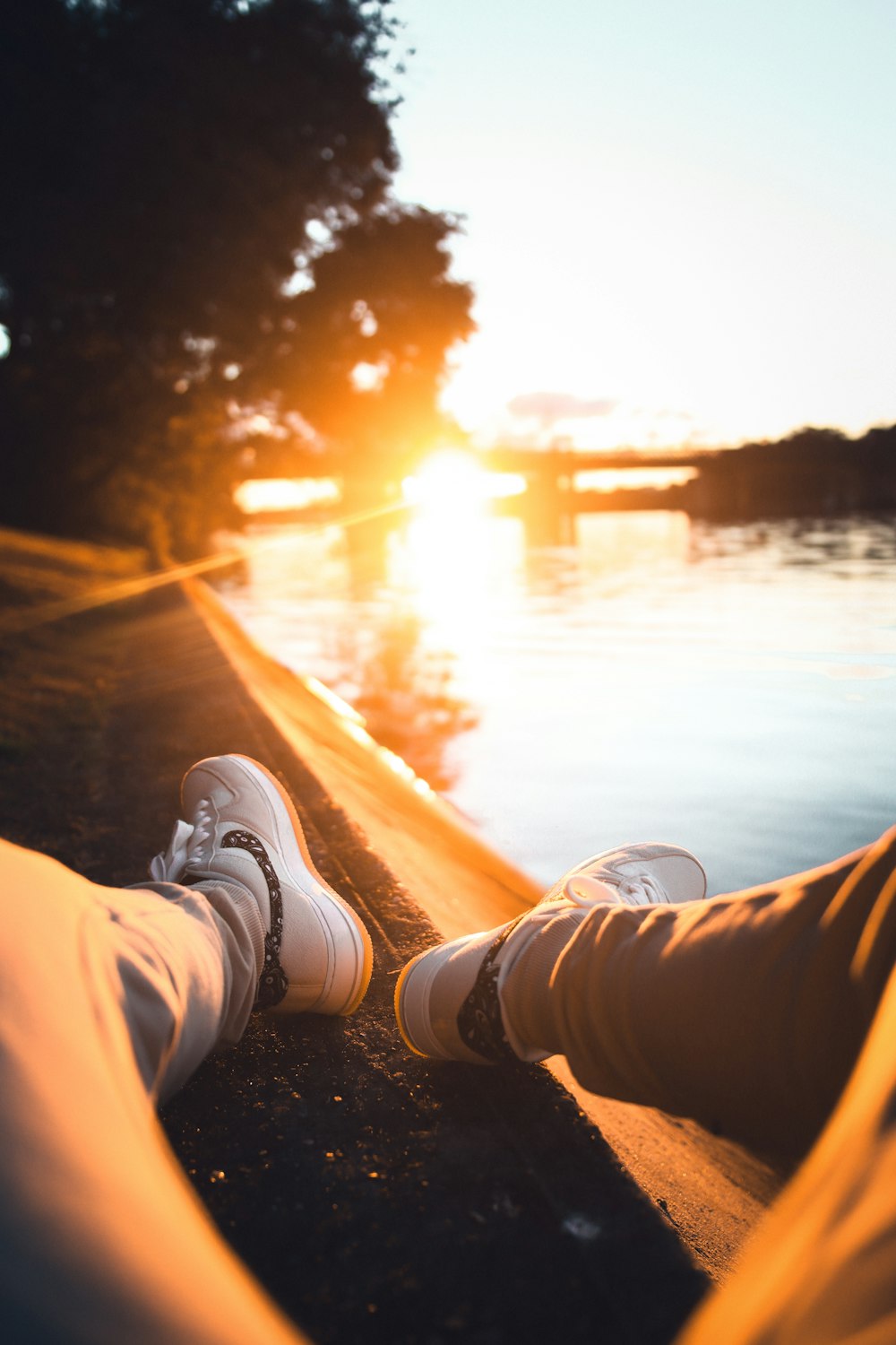 person in white pants and white sneakers sitting on rock during sunset