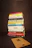 A stack of various books is neatly piled on a dark background. The titles of the books focus on topics such as business, personal development, leadership, and psychology. In front of the stack lies a wooden board with a letter 'R' engraved on it.