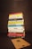 A stack of various books is neatly piled on a dark background. The titles of the books focus on topics such as business, personal development, leadership, and psychology. In front of the stack lies a wooden board with a letter 'R' engraved on it.