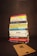 A stack of various books is neatly piled on a dark background. The titles of the books focus on topics such as business, personal development, leadership, and psychology. In front of the stack lies a wooden board with a letter 'R' engraved on it.