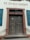 A large wooden double door with an ornate frame and chain hanging down the front. Above the doors, the words 'ST. JOSEFSHEIM' are inscribed on the wall. The building features a weathered, historical appearance with blue shutters flanking each side of the door.