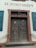 A large wooden double door with an ornate frame and chain hanging down the front. Above the doors, the words 'ST. JOSEFSHEIM' are inscribed on the wall. The building features a weathered, historical appearance with blue shutters flanking each side of the door.