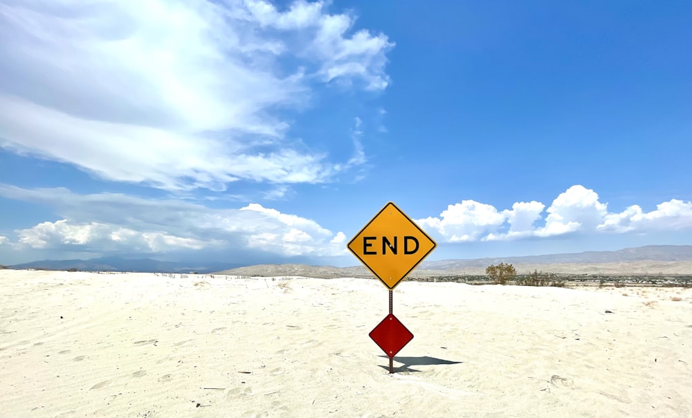 red and yellow road sign on white sand under blue sky during daytime