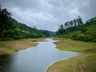 A winding river cutting through a lush green valley under soft clouds