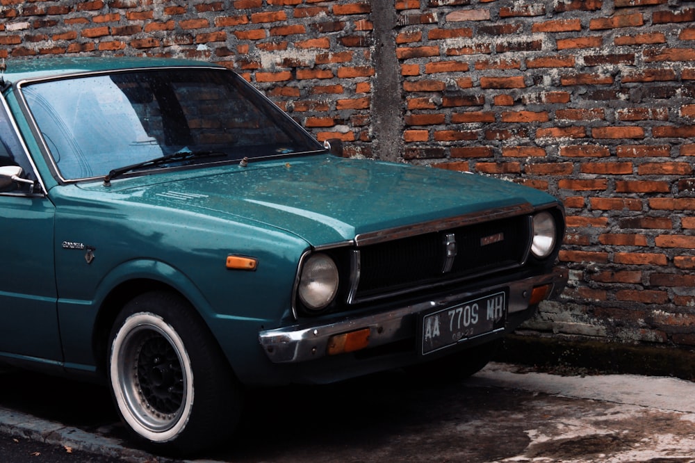 teal car parked beside brown brick wall