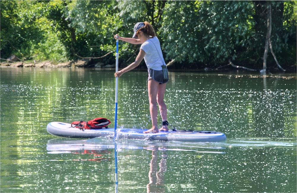 woman in white shirt and blue shorts standing on blue surfboard during daytime