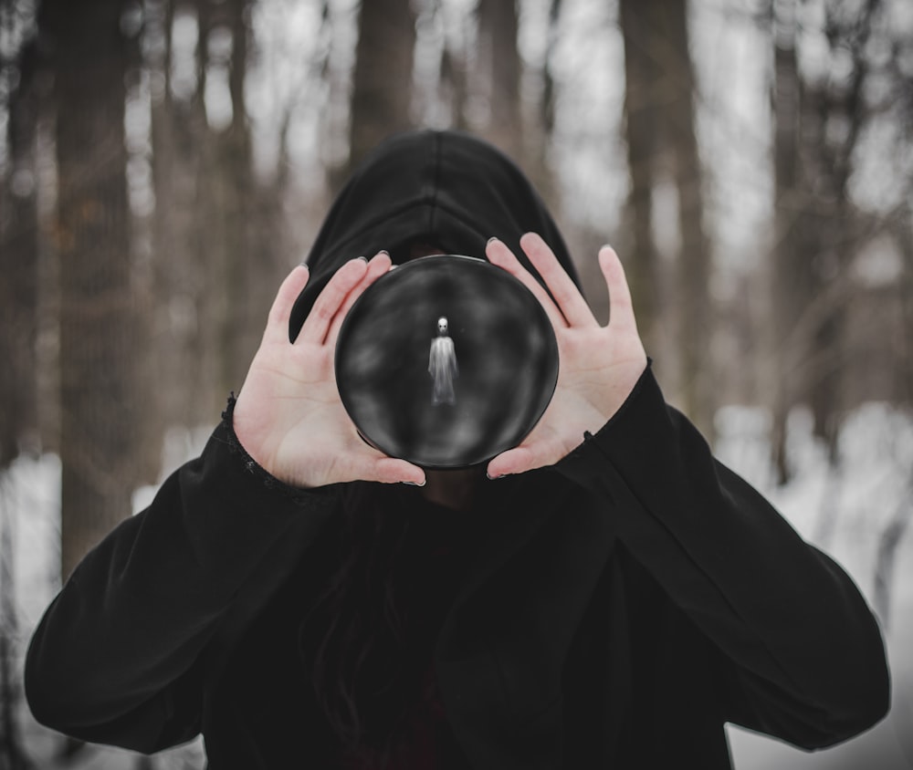 person in black hoodie covering face with black round ornament